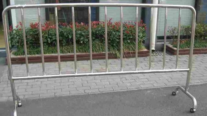 A crowd control barrier with bridge feet and four wheels stands on the concrete.